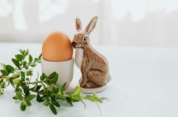 Figurka króliczka wielkanocnego postawiona obok jajka na świątecznie przystrojonym stole
