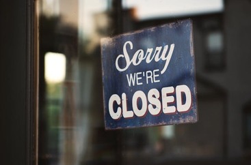 Granatowa tabliczka z napisem: sorry we're closed wisi na szklanych drzwiach.